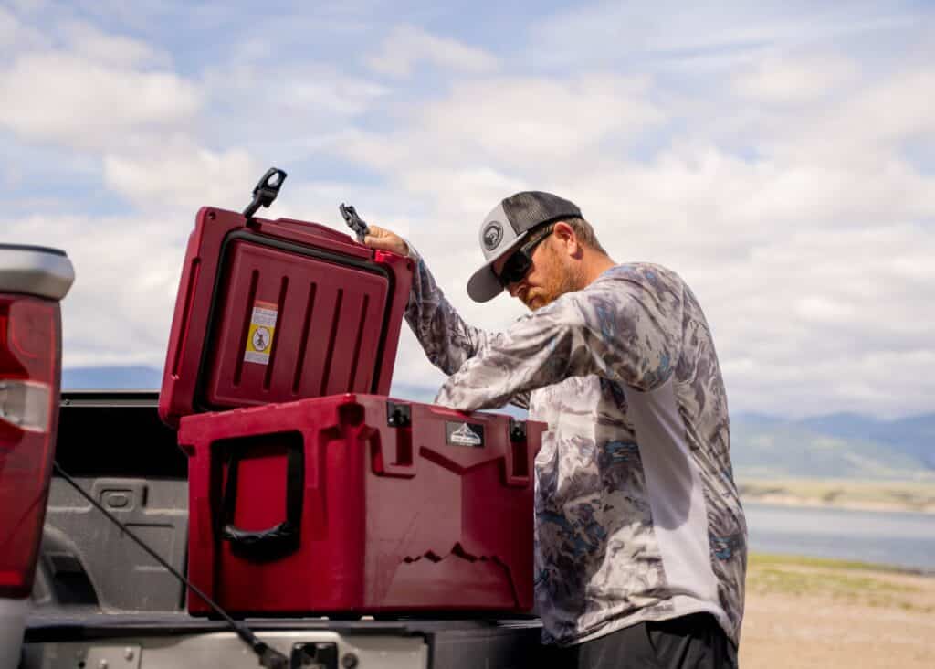 A person opening a red hard shell cooler for kayaking