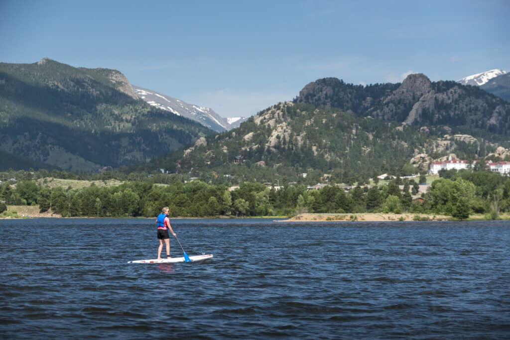 A woman standing on a kayak in the Mountian Lake Estes Colorado