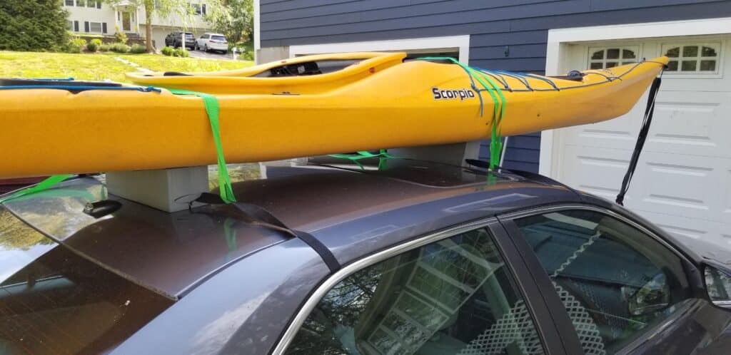 a car is carrying a kayak with the help of foam block straps