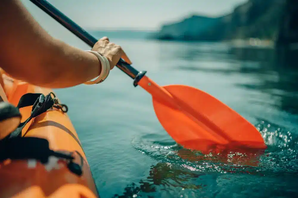 Person paddles with orange paddle oar on kayak in sea