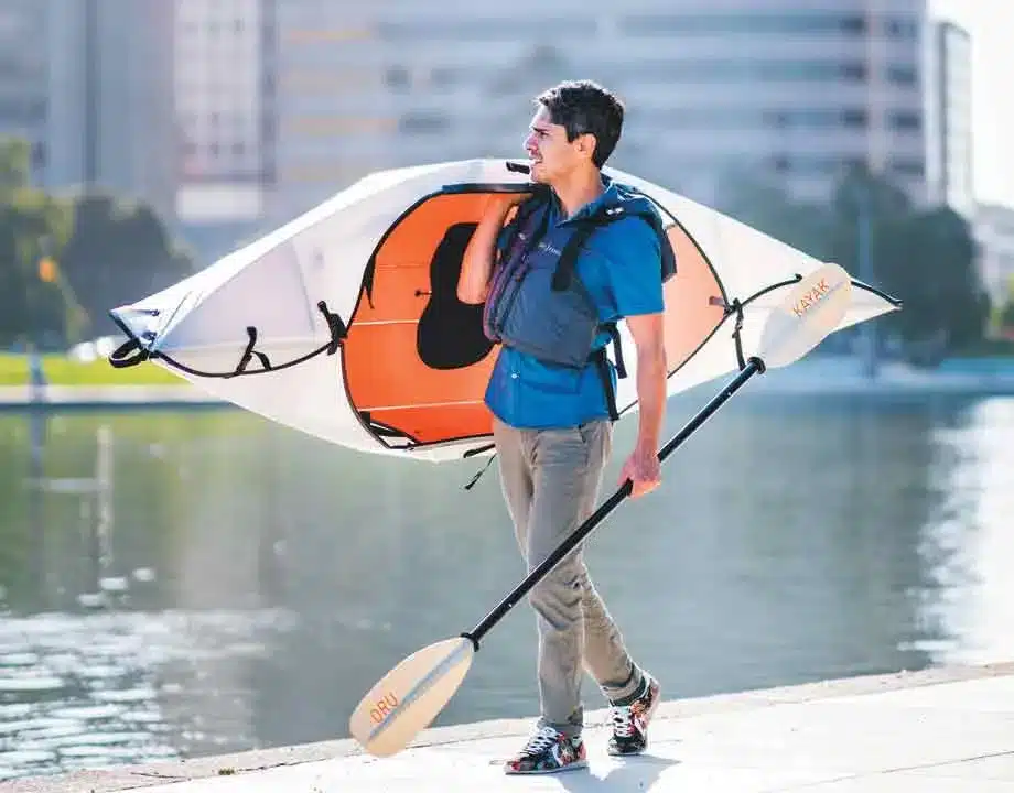 a man carrying a foldable kayak and a paddle in hand