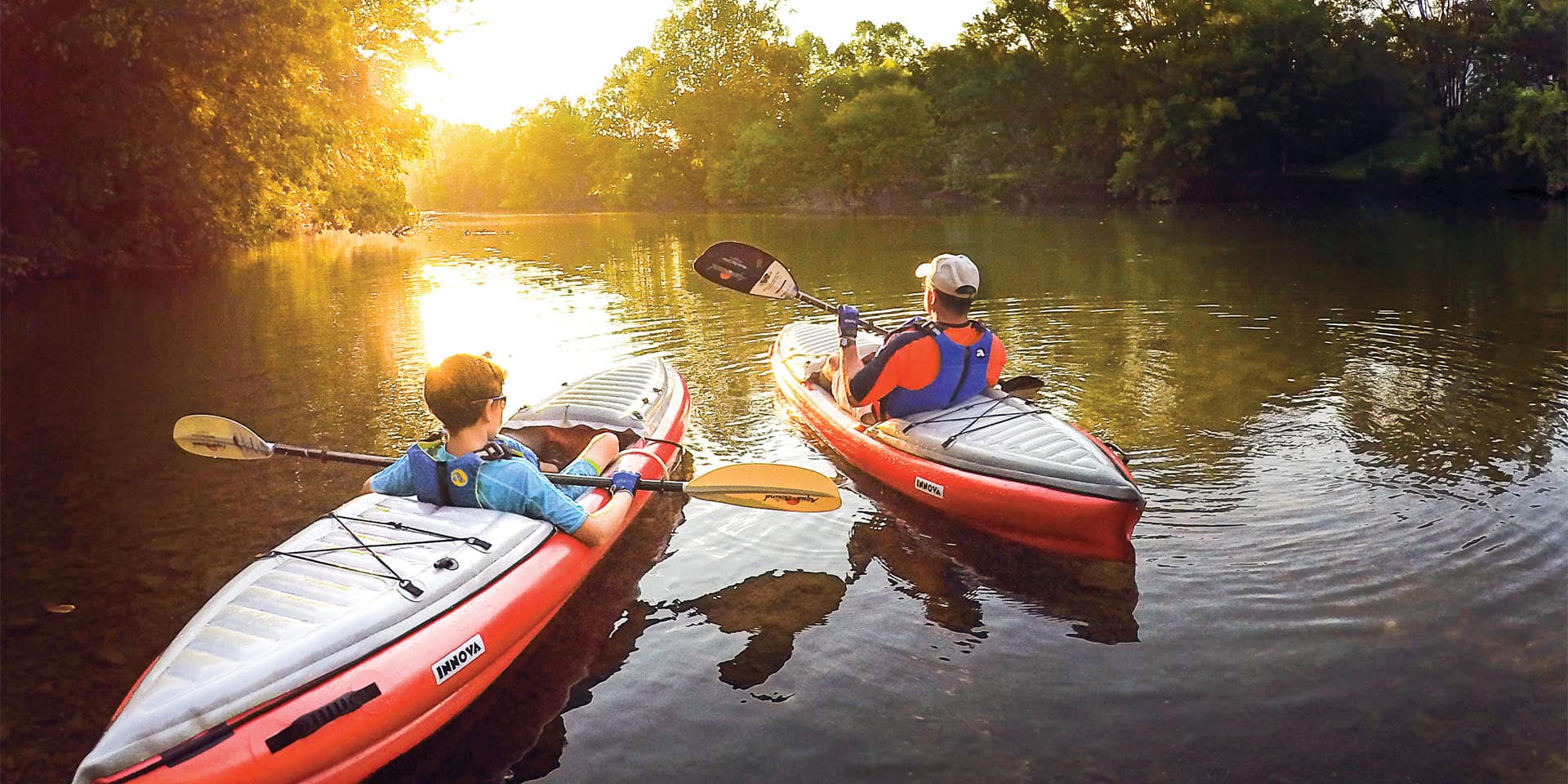 father and son kayaking in a river with sunset view