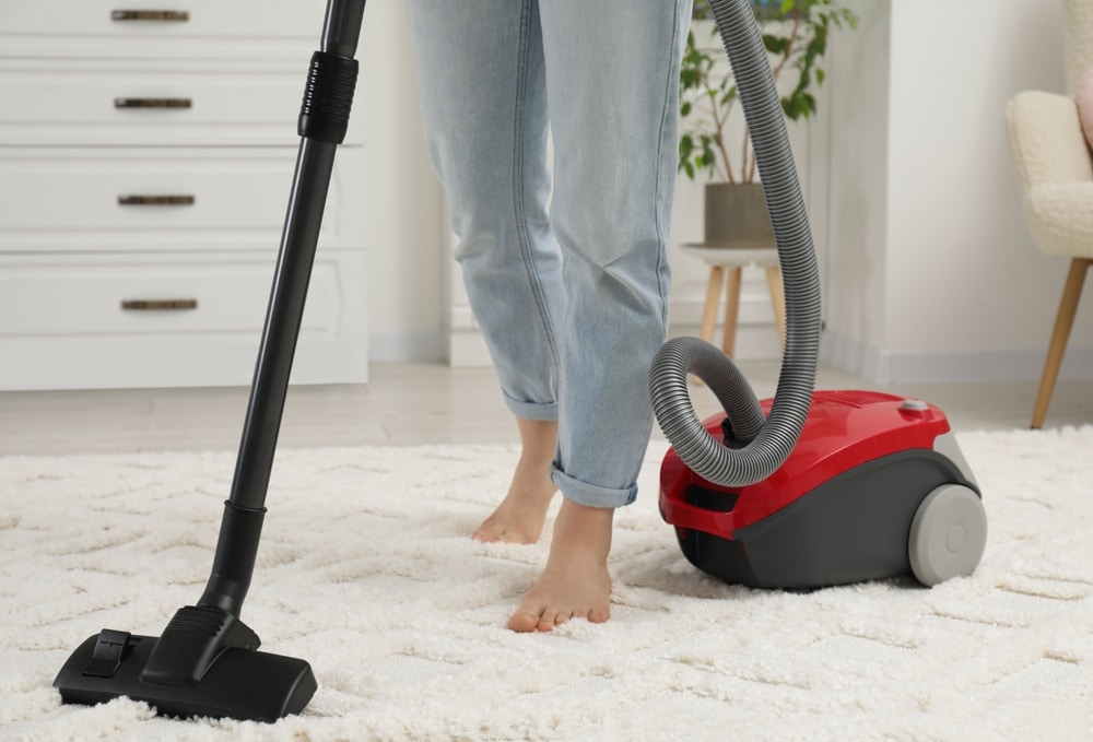 Woman Cleaning Carpet With Vacuum Cleaner At Home Closeup