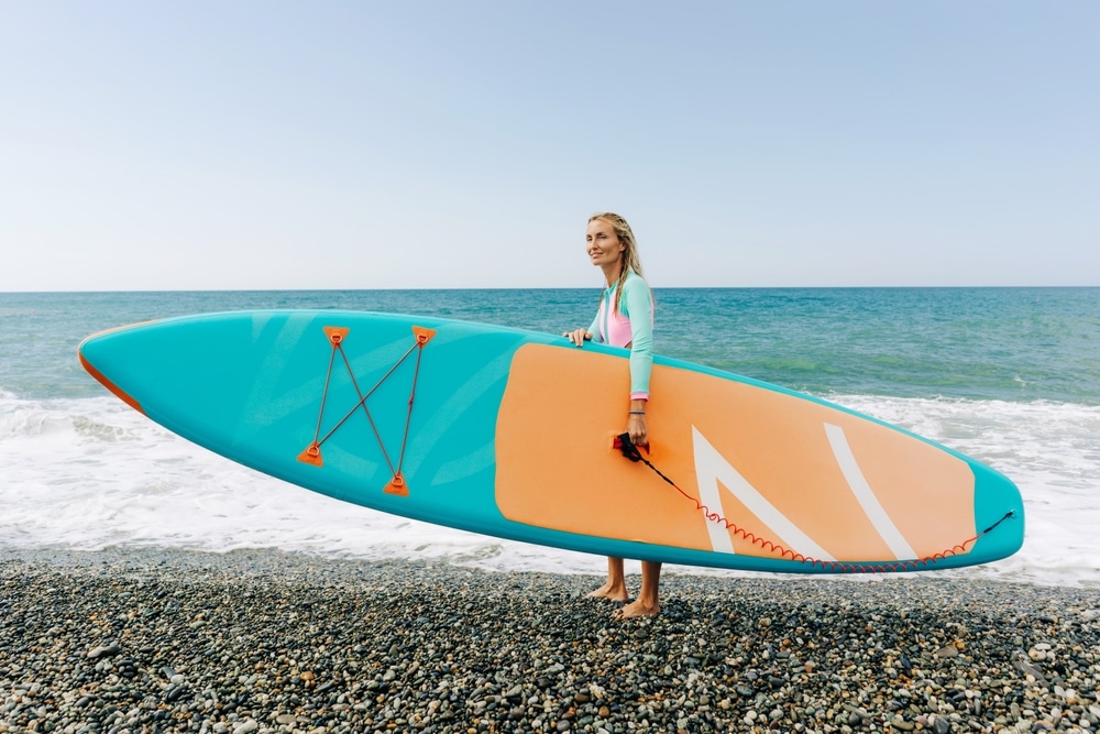 Young Athletic Blonde Woman Stands On The Beach And Holds