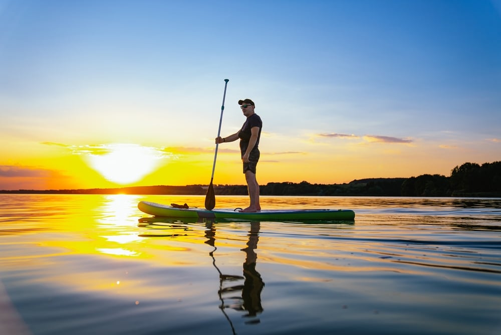 Man Paddleboarding At Sunset On A Lake A Man Stands